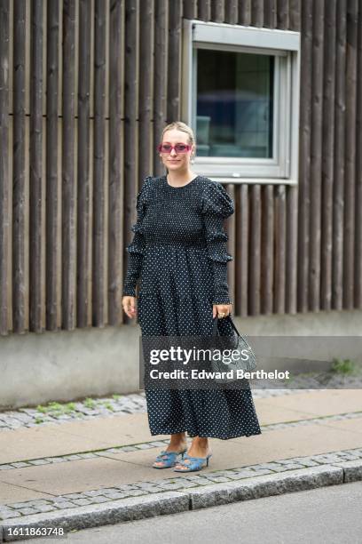 Guest wears red sunglasses, a black with white polka dors print pattern long sleeves long dress, a silver crystals handbag from Prada, blue denim...