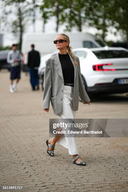 Guest wears black marble pattern sunglasses from Chanel, gold earrings, a black turtleneck ribbed pullover, a pale gray oversized blazer jacket, a...