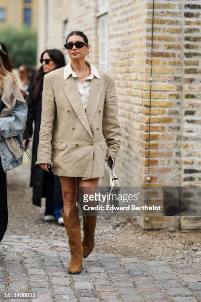 Guest wears black sunglasses, a gold necklace, a white latte shirt, a beige oversized blazer jacket as a dress, camel suede pointed / block heels...