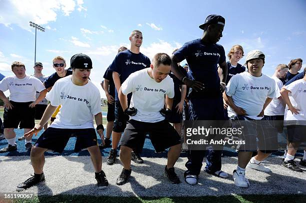 Down Syndrome football players in white t-shirts dance with Valor Christian High School football players for a warm-up at the Valor stadium in...