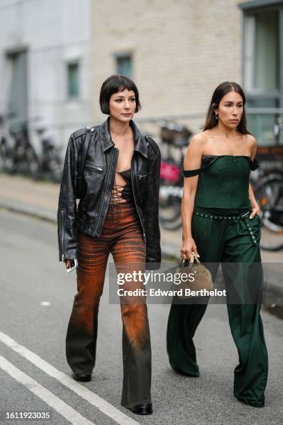 Guest wears a black shiny leather zipper jacket, a black laces front top, black and orange gradient print pattern denim flared pants, black shiny...