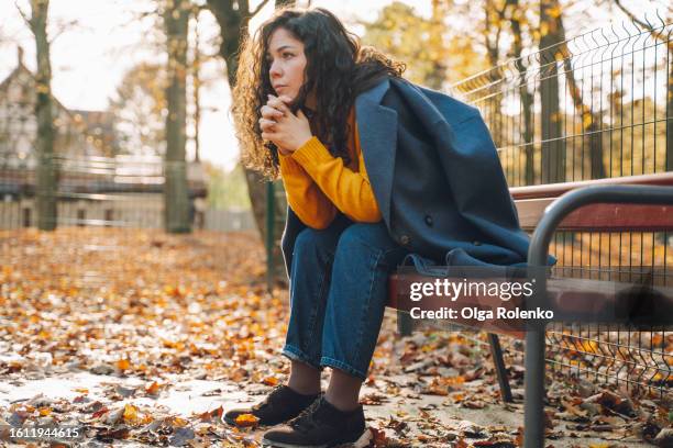 depressed brunette woman bending on the bench with head in hands. feeling sorrow and pain in autumn park - autumn sadness stock pictures, royalty-free photos & images