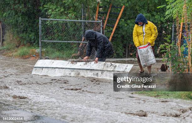 Rafael Nunez right, with Isabel Ramirez carries bags of fertilizer to prop up a piece of roofing to try and divert flood waters on 70th Avenue from...
