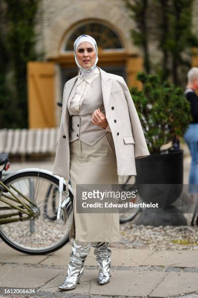 Guest wears a white and silver silk scarf as a headband, a beige checkered print pattern buttoned gilet, a matching beige checkered print pattern...
