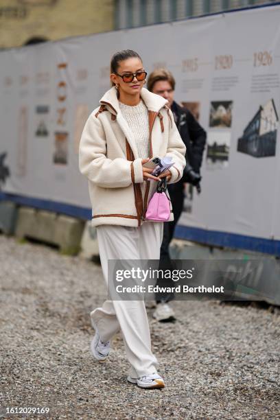 Guest wears brown and orange sunglasses, a white wool pullover, a white latte fluffy sheep fur with camel leather borders large coat, a pink nylon...