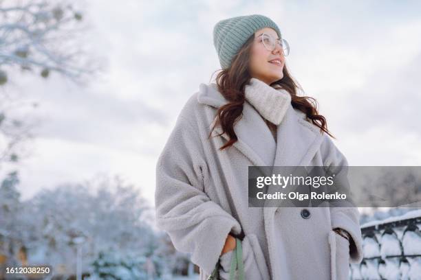 frosty adventure on winter streets. joyful brunette woman with hands in coat pockets resting winter park during strolling outdoors - public park design stock pictures, royalty-free photos & images