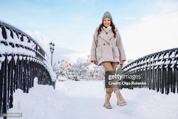 winter snowing and strolling along the bridge: smiling woman in glasses in warm clothes taking walk by frost bridge in winter - winter coat stock pictures, royalty-free photos & images