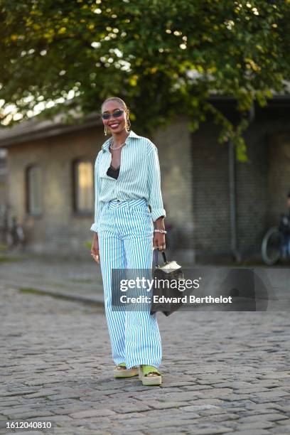 Guest wears black sunglasses from Chanel, silver earrings, a silver chain necklace, a pale green and white striped print pattern shirt, a black bra...