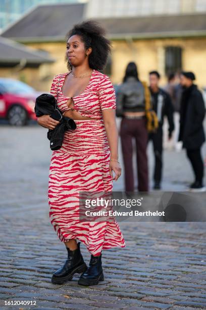 Guest wears gold earrings, a gold necklace, a beige and red zebra print pattern squared neck / short sleeves / cut-out chest / long dress, a black...