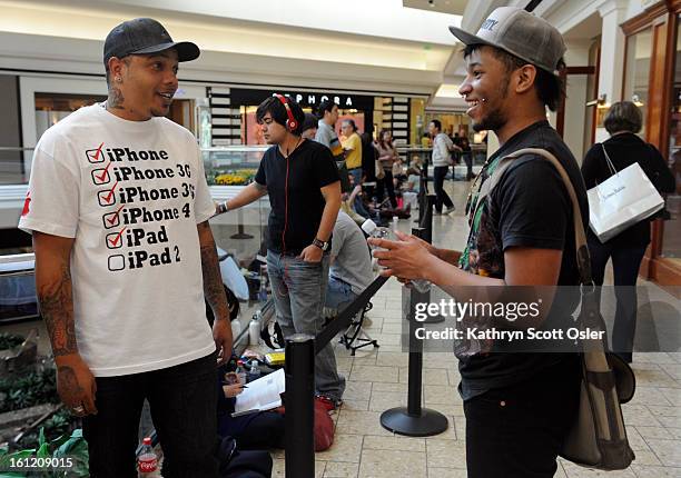 Lorenzo Johnson, left, wears a t-shirt depicting all the Apple products he has stood in line to buy on their opening day of sales. He says the...
