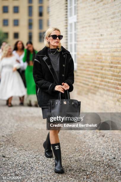 Guest wears black sunglasses, a dark gray wool short t-shirt dress, a black sheep and suede long jacket, a black shiny leather Birkin handbag from...