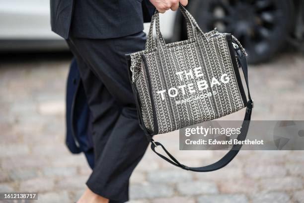 Guest wears a black suit, a black and white print pattern fabric Tote-Bag handbag from Marc Jacobs, outside Munthe, during the Copenhagen Fashion...