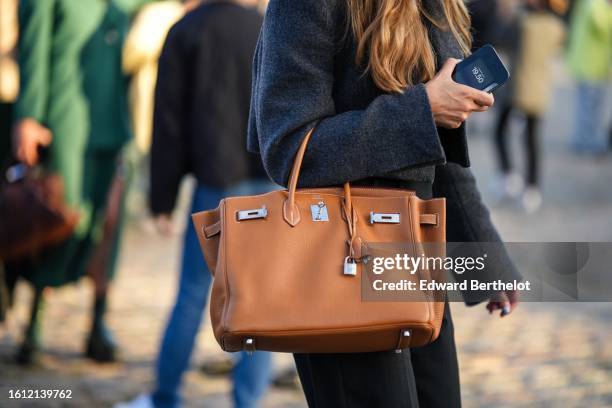 Guest wears a dark gray wool jacket, black suit pants, a camel shiny leather Birkin handbag from Hermes , outside Ganni, during the Copenhagen...