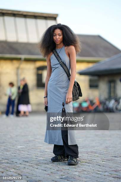 Guest wears a pale gray halter-neck / sleeveless long slit dress, a black denim large crossbody bag, black large pants, black shiny leather sneakers...