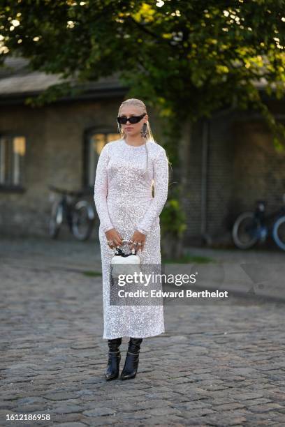 Guest wears black sunglasses, black stras pendant earrings, a white silver sequined long sleeves / long dress, silver rings, a white embossed leather...