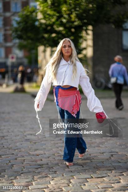 Guest wears a white cropped shirt, navy blue denim large wide legs pants, a red shiny leather handbag, a red and white striped print pattern short...
