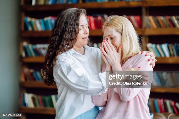empathy and therapy healing with stressed woman. compassionate mental health professional hugging, support distressed female patient in doctor office: brunette curly haired therapist consoles and embraces woman - stress test stockfoto's en -beelden