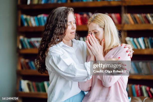 empathy and therapy healing with stressed woman. compassionate mental health professional hugging, support distressed female patient in doctor office: brunette curly haired therapist consoles and embraces woman - showing empathy stock pictures, royalty-free photos & images