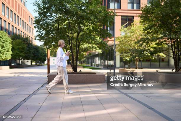 woman in casual style  walking on street with smart phone in hand - calling on the side road stock pictures, royalty-free photos & images