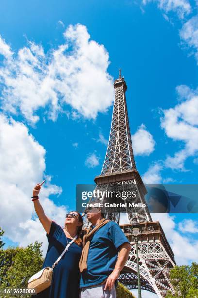 portrait of senior couple by the eiffel tower - voyageur homme devant monument photos et images de collection