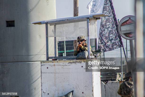 An Israeli soldier stands guard at a military post while others are searching vehicles passing near the area during intensive operations to search...