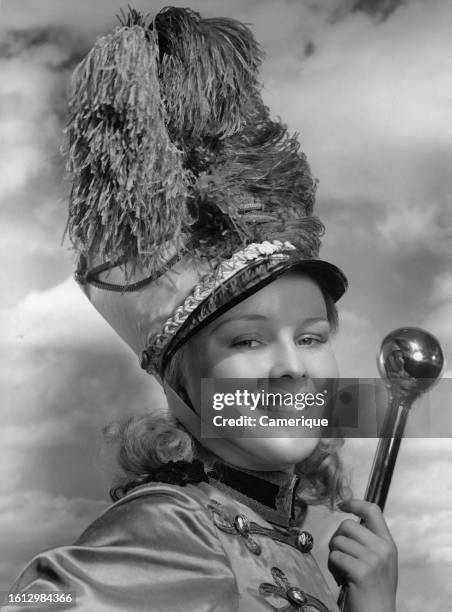 Close-up shot of a female majorette wearing the outfit the hat with the pom-pom on top carrying a baton as she smiles at the camera with the cloudy...