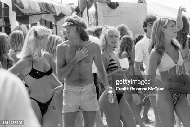 American surfer and skateboarder George Trafton, wearing shorts, an Instinct visor and holding a Coca-Cola can stands in the midst of the competitors...