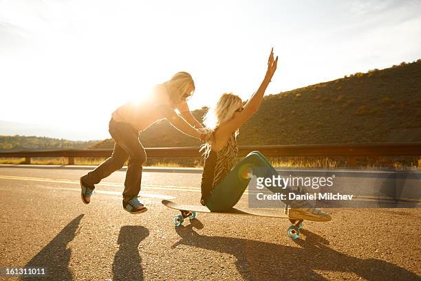 a guy pushing a girl on a skateboard. - woman longboard stock-fotos und bilder