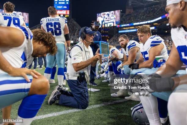 Mike Solari offensive line coach of the Dallas Cowboys shows players a microsoft surface on the sidelines during a preseason game at Lumen Field on...