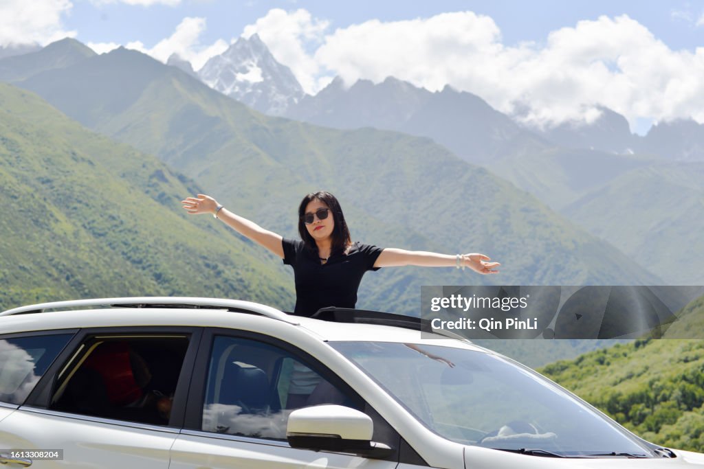 A woman enjoys the view from the sunroof of a car