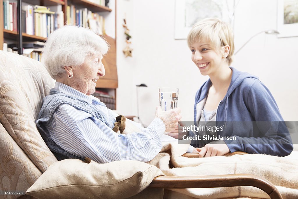 Caregiver giving glass of water to senior woman