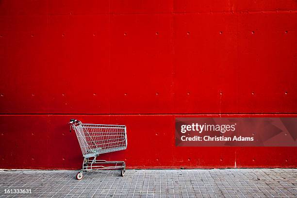shopping cart in front of a red wall - winkelwagentje stockfoto's en -beelden