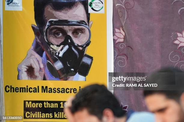 People sit across from a poster depicting Syria's President Bashar al-Assad in a gas mask during an event in the rebel-held northern city of Afrin,...