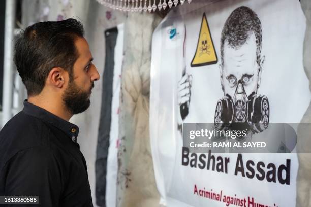 Man looks at a poster depicting Syria's President Bashar al-Assad in a gas mask during an event in the rebel-held northern city of Afrin, on August...