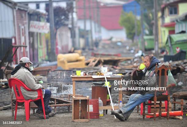 Men sit in a street devastated by the tsunami in Talcahuano, Chile, March 1, 2010. Chile's earthquake toll soared past 700 on Sunday as rescuers...