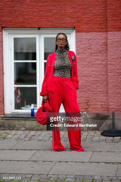 Guest wears black glasses, a brown / beige and black leopard print pattern turtleneck t-shirt, a neon red zipper sport sweater, matching neon red...