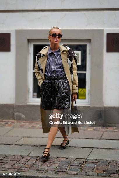 Guest wears black sunglasses, gold earrings, a navy blue and white striped print pattern shirt, a beige long trench coat, a dark brown and pale gray...