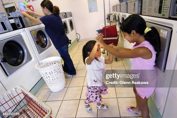 DENVER, COLORADO, JULY 10, 2006--Monica Gonzalez of Denver feeds a washer while her daughters, Skye <cq> , 3, center, and Mariah <cq> , 8, start a game of Roman knuckles at the Magic Laundry and Dry Cleaners in south Denver. Coin-op connoisseurs say they DENVER, COLORADO, JULY 10, 2006--Monica Gonzalez of Denver feeds a washer while her daughters, Skye <cq> , 3, center, and Mariah <cq> , 8, start a game of Roman knuckles at the Magic Laundry and Dry Cleaners in south Denver. Coin-op connoisseurs say they