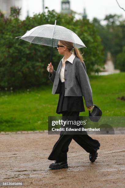 Guest wears black sunglasses, a white latte shirt, a gray blazer jacket, a black pleated / accordion short skirt, a black shiny leather handbag from...