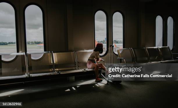 a little girl sits in an airport, waiting for a flight. - windows stock pictures, royalty-free photos & images