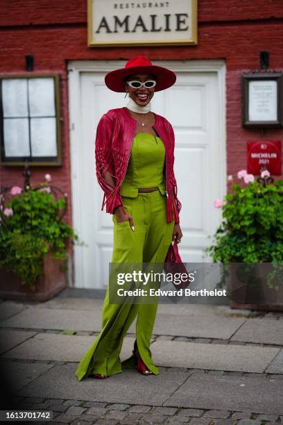 Guest wears a red suede large hat, white sunglasses, a white latte scarf, a red shiny leather fringed jacket, a gold necklace, a green shoulder-off...