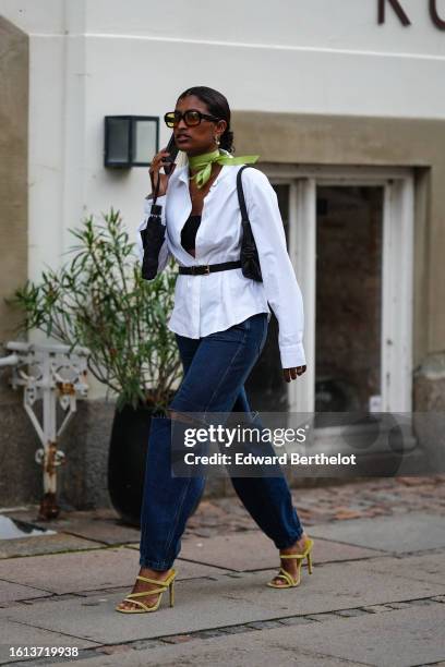 Guest wears black sunglasses, a green silk scarf, a white shirt, a black shoulder-off top, a black shiny leather shoulder bag, a black shiny leather...