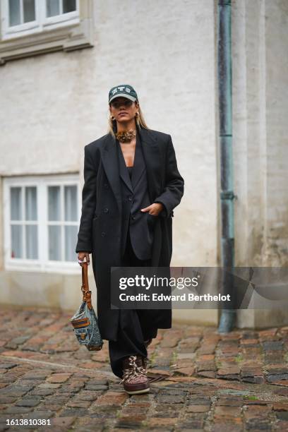 Guest wears a dark green denim with white embroidered NYC cap from Anine Bing, gold earrings, a brown silk flower necklace, a black shoulder-off top,...