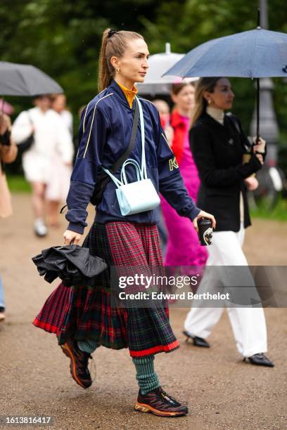 Guest wears a yellow turtleneck pullover, a navy blue with yellow embroidered pattern zipper sport sweater, a pale blue matte leather crossbody bag...