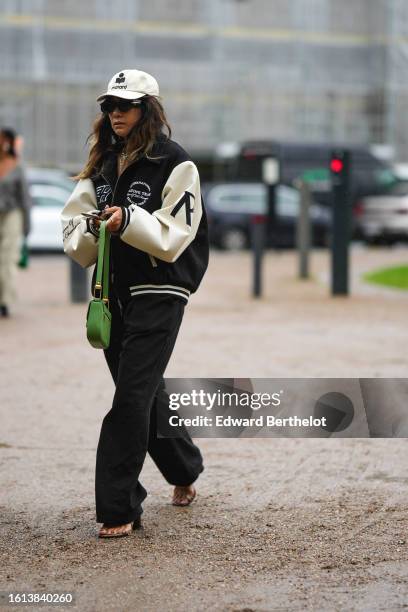 Guest wears a white with black embroidered logo pattern cap from Isabelle Marant, black sunglasses, a black felt wool / white leather sleeves teddy...