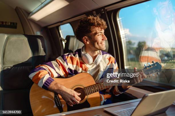 young man playing a guitar during a train ride - passenger muzikant stockfoto's en -beelden