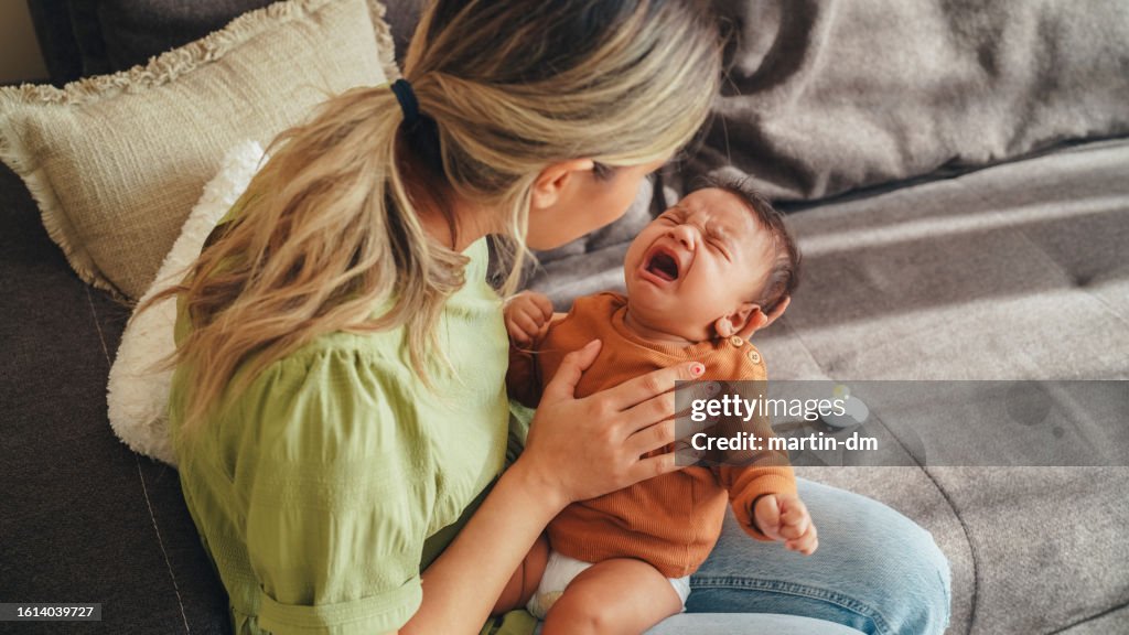 Young mother tries to calm her screaming newborn baby