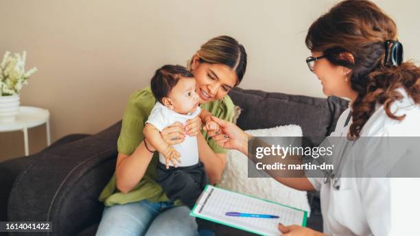 doctor visiting young mother at home for routine checkup of the newborn - mid wife stock pictures, royalty-free photos & images