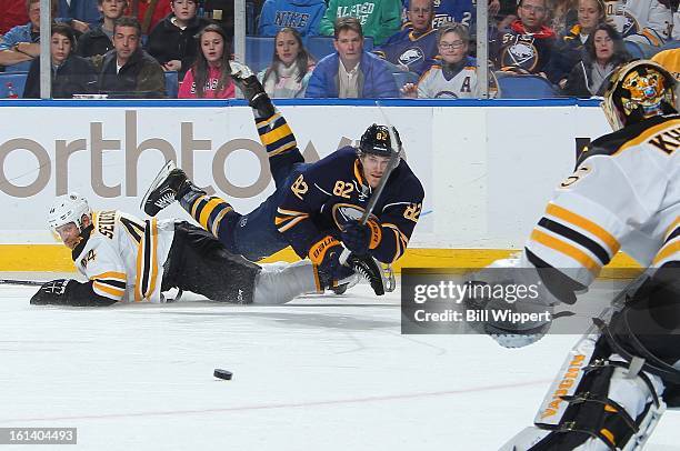 Marcus Foligno of the Buffalo Sabres sends a pass to the front of the net guarded by Anton Khudobin of the Boston Bruins while being upended by...