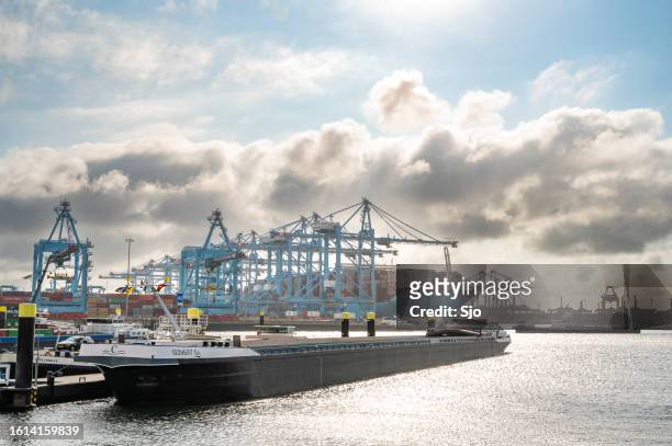 shipping container terminal in the port of rotterdam with a barge in the foreground - barge stock pictures, royalty-free photos & images